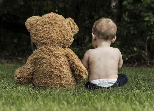 Teddy bear and toddler sat next to each other in a garden